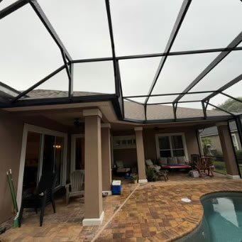 View from inside a finished pool enclosure toward a covered lanai and paver deck