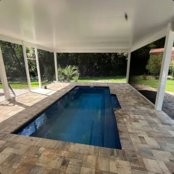 White insulated patio cover running the length of a lap pool over paver decking